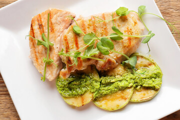 Tasty grilled chicken meat, zucchini and pesto sauce on table, closeup