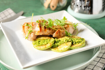 Plate with tasty grilled chicken meat, zucchini and pesto sauce on color background, closeup