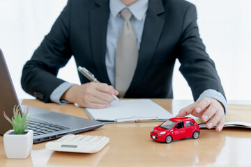 A car on desk envelope with man signing purchase documents in background. while hand complete the...