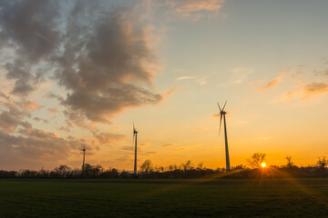 Fototapeta na wymiar three windmills on a green field in the nature while sunset