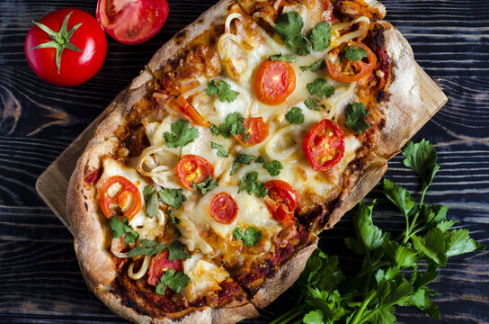 Fresh pinsa with tomatoes and herbs on a dark wooden background top view. Pinsa home cooking. Pizza pastries