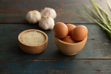 Multiple eggs in a cup with garlic and onions lay on a vintage wooden floor.