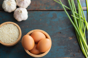 Multiple eggs in a cup with garlic and onions lay on a vintage wooden floor.