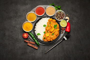 Plate of Traditional Chicken Curry and set of spices on dark concrete background