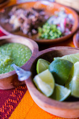 Bowls of lime slices and hot sauce on red and orange tablecloth