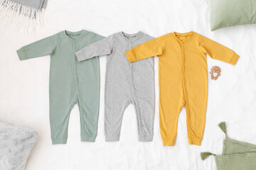 Three children's jumpsuit in green yellow and grey color, pillows and blanket lying on a white background. Baby clothes, flat lay.