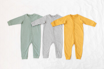 Three children's jumpsuit in green yellow and grey color lying on a white background. Baby clothes, flat lay.