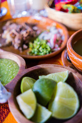 Bowls of lime slices, green sauce, and lamb broth on colorful tablecloth