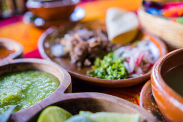 Bowls of lime slices and green sauce, and plate of lamb meat on table