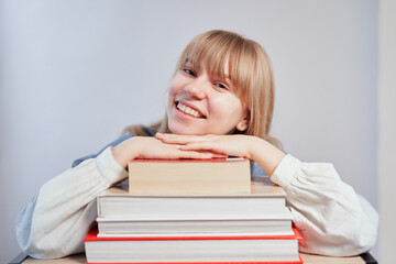 Young school girl with books in class with copy space. Attractive smiling blonde student relaxing lying on stack of books. Homeschooling or back to school concept. High quality photo