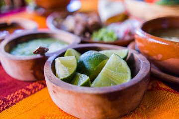 Fototapeta na wymiar Bowls of lime slices, green sauce, and lamb broth on colorful tablecloth
