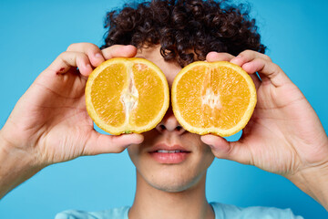 Cheerful guy holding oranges near his eyes close-up blue background