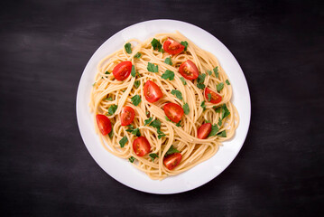 Pasta spaghetti with cherry tomatoes, fried sausage and parsley  in white plate on a black  background.