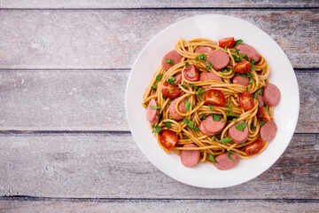 Pasta spaghetti with cherry tomatoes, fried sausage and parsley  in white plate on a light background.