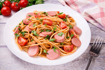 Pasta spaghetti with cherry tomatoes, fried sausage and parsley  in white plate on a light background.