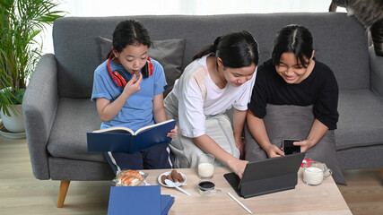 Three young girl having fun with device at home.