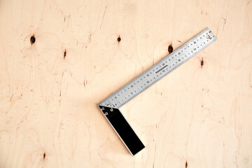 Steel framing set square on a wooden background. L-square instrument. Right angle. Silver color. Copy space. Plywood backdrop. Building rule. Measurement tool. Carpentry device. Triangle 90 degrees