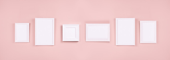 Abstract interior of gallery with set of many different white blank photo frames for text, design, poster, pictures hanging on pastel pink wall, web banner. Mock up for display portfolio.