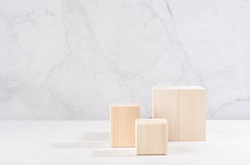 Wooden beige podiums of different cubes on white wood table and marble wall. Showcase for cosmetic products, goods, shoes, bags, watches.