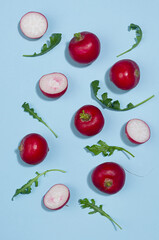 Fresh summer vegetables - radish and arugula with shadow on blue background, top view.