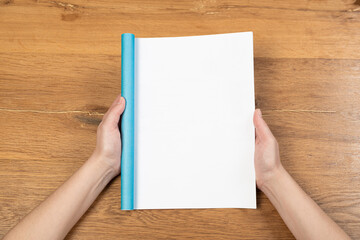 Fototapeta premium Woman holding brochure with blank cover on wooden background, top view. Mock up for design