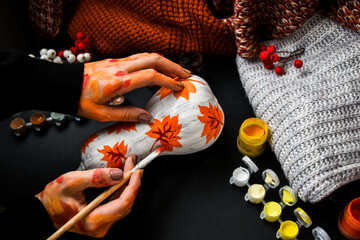 DIY. Do it yourself. Woman paints thanksgiving decorations on orange pumpkin for Halloween. Autumn...