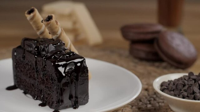 Delicious liquid chocolate dripping from a freshly baked cake slice - sweet food. Closeup shot of yummy chocolate pastry with choco chips  biscuits  roll wafer sticks  and hot chocolate melt drink