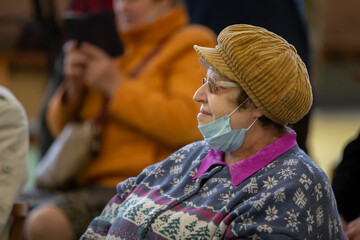 An elderly woman in a medical mask at an event during a coronavirus infection.