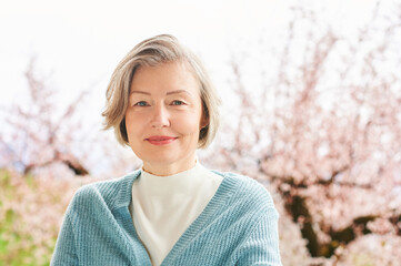 Spring portrait of beautiful and elegant middle age woman posing against pink blooming tree - 430742437