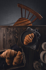 Croissants with chocolate in a wicker basket and a plate on a dark wooden table with a seat. Top view. Delicious dessert for breakfast with coffee or tea. Vertical orientation.