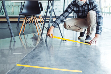 Business man Tape being attached behind social distancing signage on office floor during COVID-19...