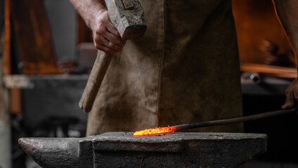 Blacksmith working metal with hammer on the anvil in the forge
