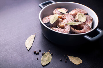 Slices of lightly salted mackerel fish with allspice and bay leaf on a black wooden table.