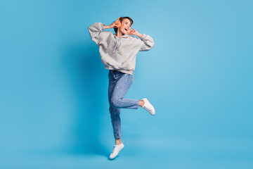 Full length photo portrait of woman jumping up with headphones isolated on pastel blue colored...