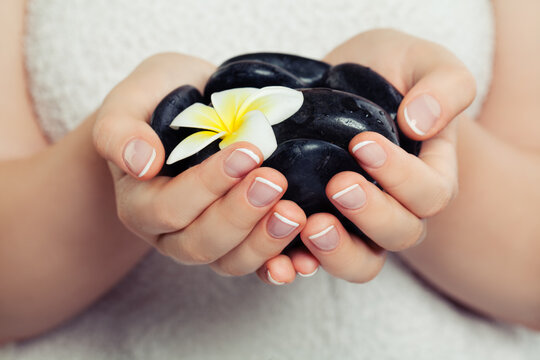 Spa woman hands with black massage stones and beautiful tropical flower
