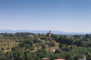Fototapeta na wymiar Un village italien en Toscane sur le sommet d une colline par une belle journée estivale, le ciel est bleu, les montagnes se distinguent au loin.