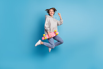 Fototapeta premium Full length body size photo of girl jumping up holding skate board gesturing like winner isolated vivid blue color background