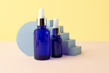 Two cosmetics bottles from blue glass with droppers.Isometric pastel background.Empty geometrical podiums behind.