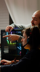 Man gamer teaching his girlfriend playing space shooter video game on RGB powerful personal computer. Pro cyber woman with headset performing video games streaming from home during online tournament