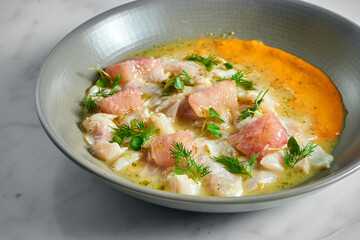 Peruvian cuisine dish - seabass ceviche with grapefruit and yellow sauce, served in a grey plate on a marble background. Restaurant seafood.