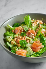 Fresh salad with salmon, delicate cheese, peanuts and mint in a gray bowl on a white marble background