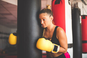 Woman in boxing gloves standing by the boxer bag.