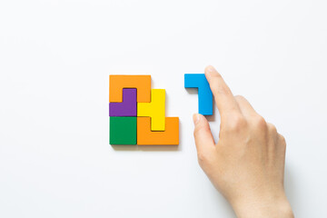 Naklejka premium Set of color blocks puzzle pieces and hand holding last one piece on white background. Creative thinking, idea, problem solving, success concept. top view