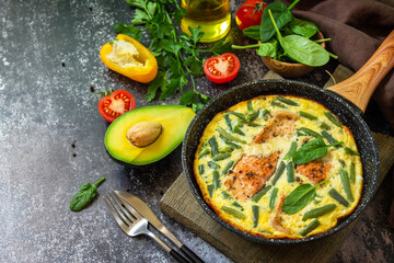 Breakfast or lunch snack concept. Rustic omelet (omelette, Scrambled)  with salmon fillet and green beans in a frying pan on a stone background. Copy space.