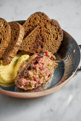 Delicious appetizer, beef steak tartare with yellow sauce and rye bread, served in a copper plate on a marble background.