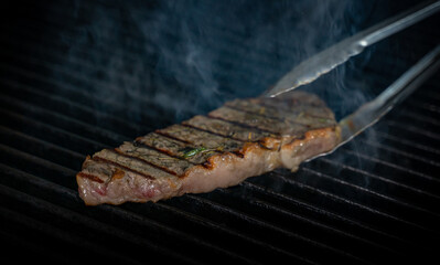 Striploin beef tip getting grilled on a barbeque grill. GRILLING