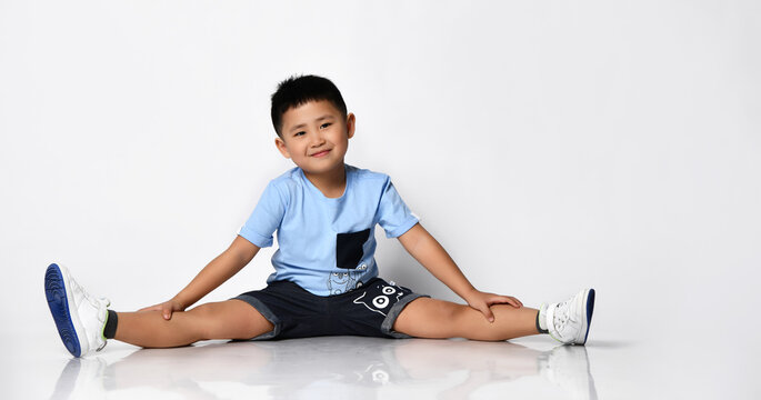 Little asian preteen school boy in summer blue t-shirt black denim shorts with funny monsters print sitting on floor looking at camera studio shot. Children trendy outfit, fashion style advertising