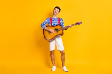Full size photo of young handsome happy positive smiling dreamy man playing guitar isolated on yellow color background