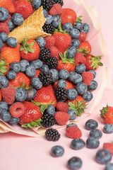 Edible bouquet of fresh berries, blueberries, raspberries, strawberries, hedgehog on a pink background with scattered berries. View from the top .Close-up .Concept of a useful gift, 