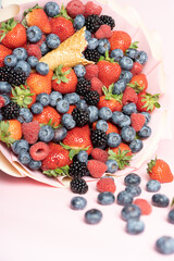 Edible bouquet of fresh berries, blueberries, raspberries, strawberries, hedgehog on a pink background with scattered berries. View from the top .Close-up .Concept of a useful gift, 